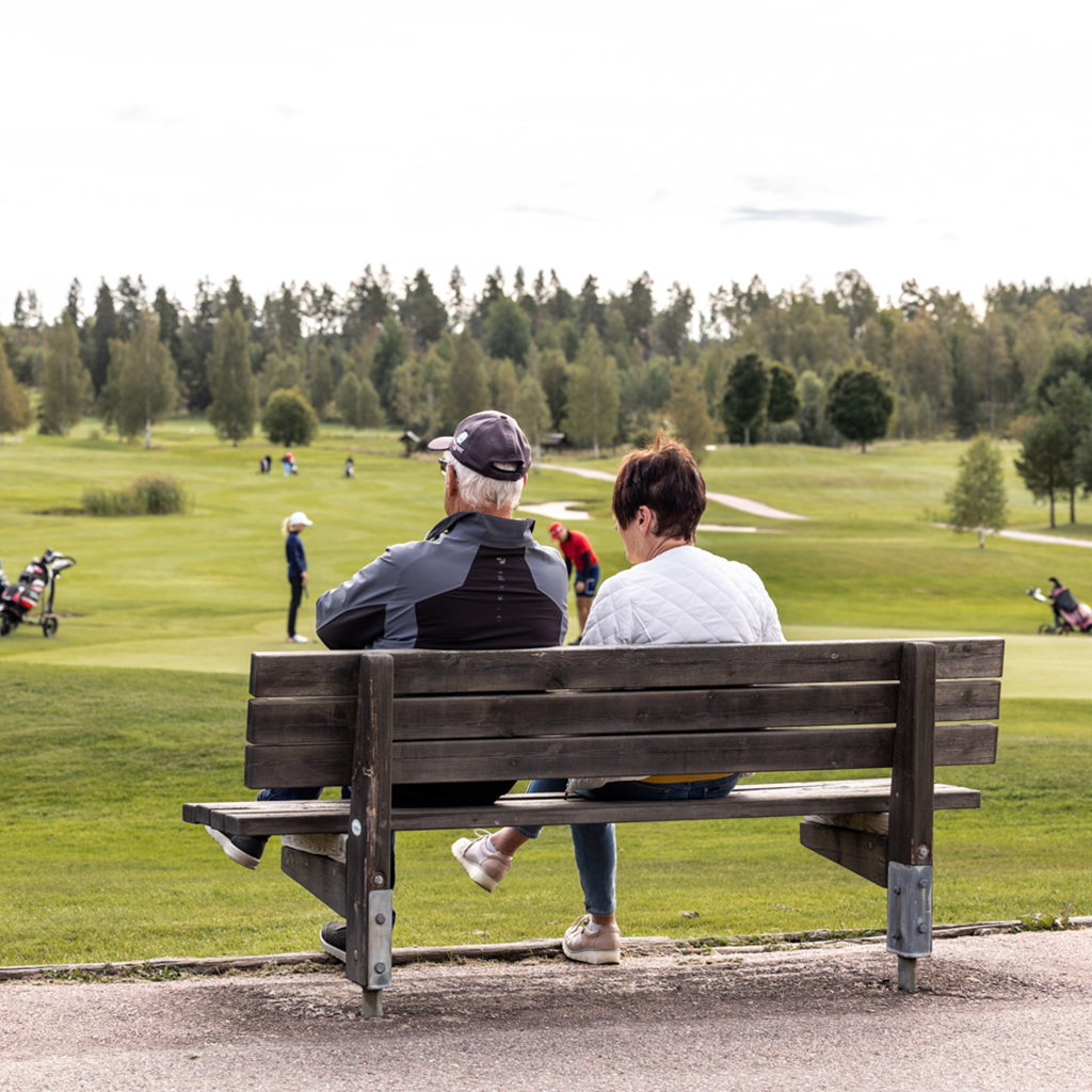 Ett äldre par sitter på en bänk vid en golf bana