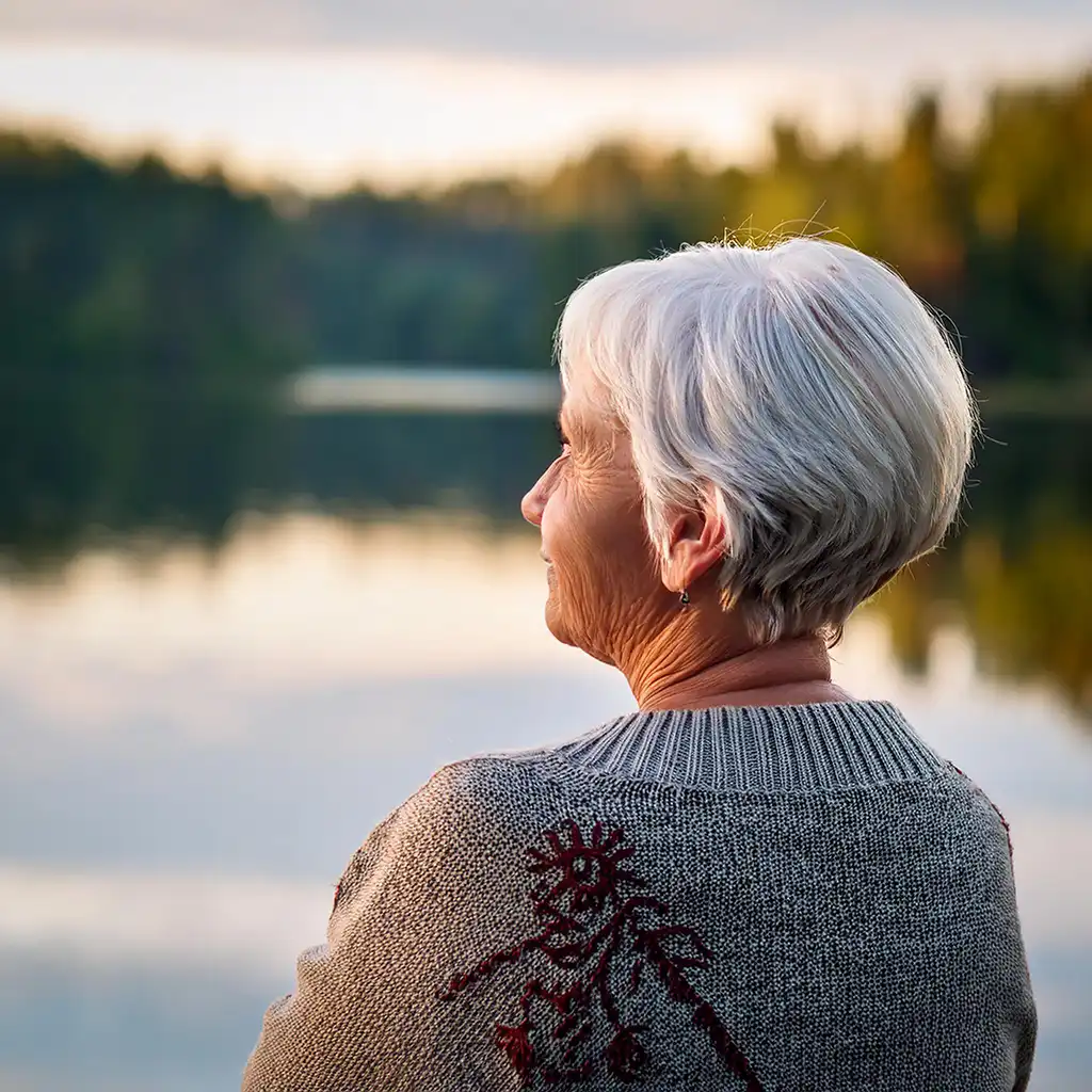 en äldre kvinna står vid en sjö och blickar ut hon är ca 60 år gammal